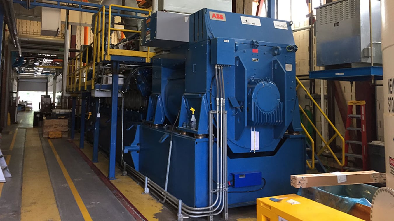 Large blue industrial electric motor installed inside a facility with connected equipment, electrical cabinets, piping and access platforms.