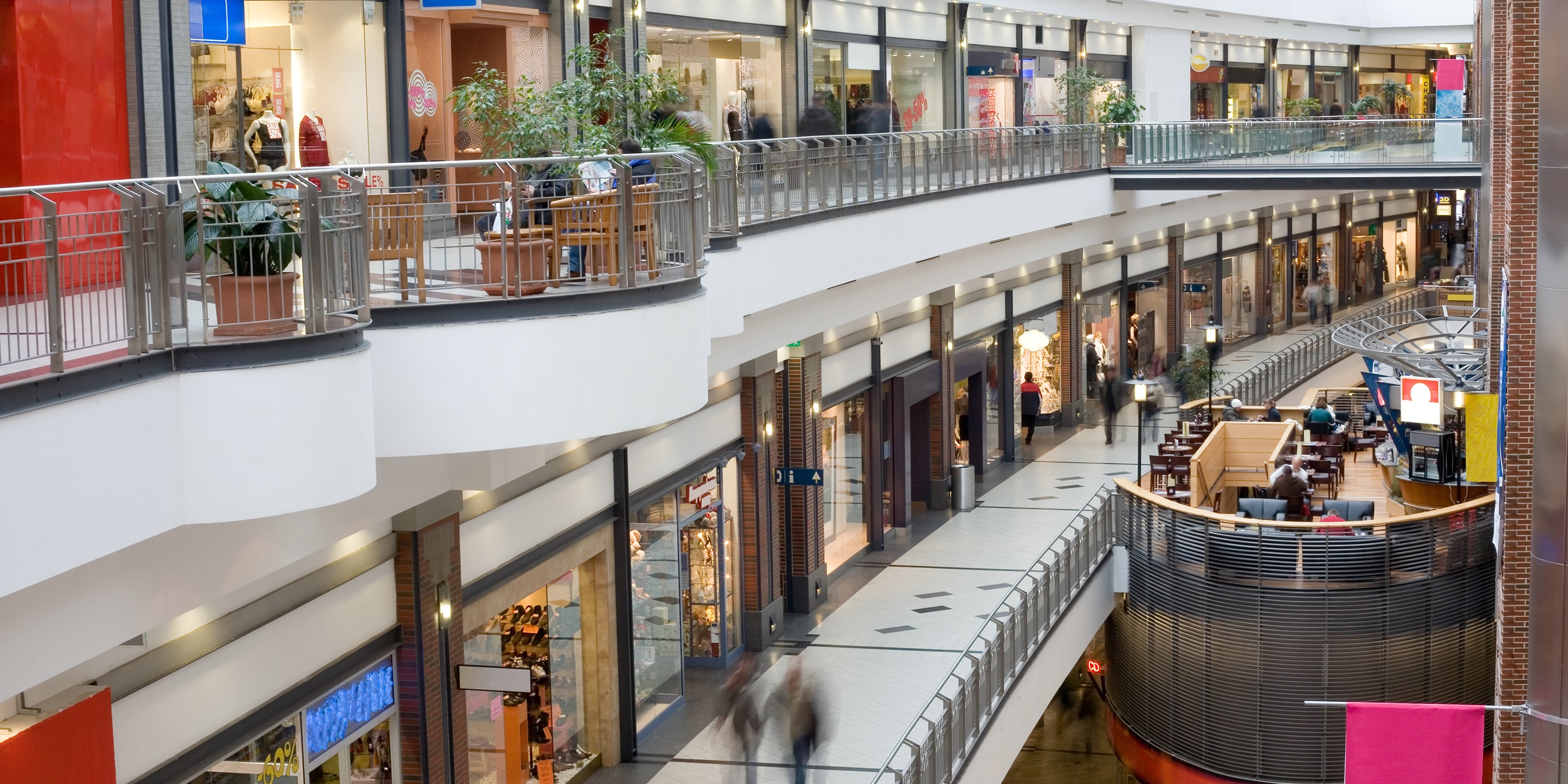 Interior view of a shopping mall featuring multiple retail stores, walkways, seating areas, and open architectural design across levels.
