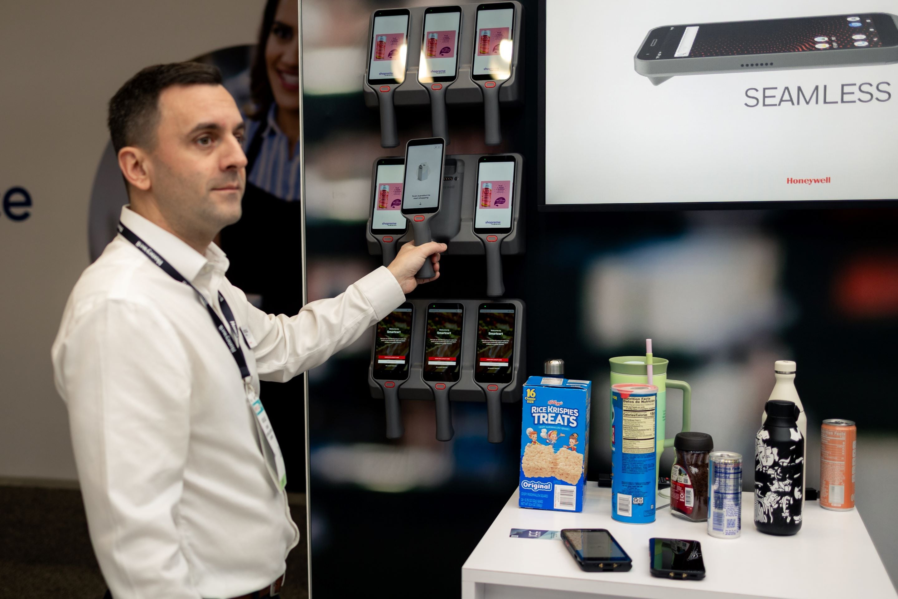 A person interacts with a display of mobile devices showcasing products, with a countertop featuring various food and drink items.