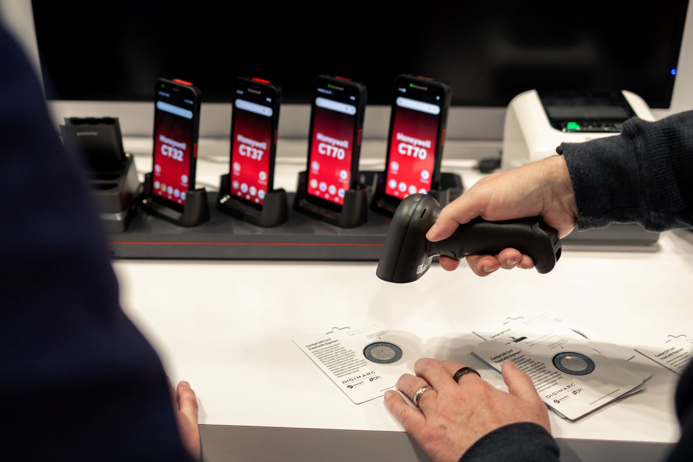 A person scans product tags with a barcode reader at a display featuring multiple mobile devices.